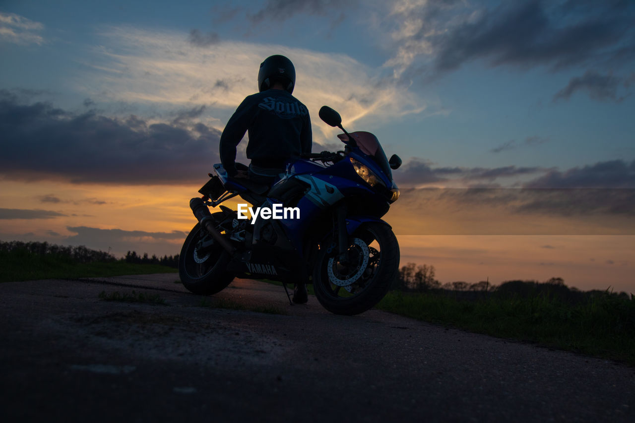 Low angle view of man by motorcycle against sky during sunset