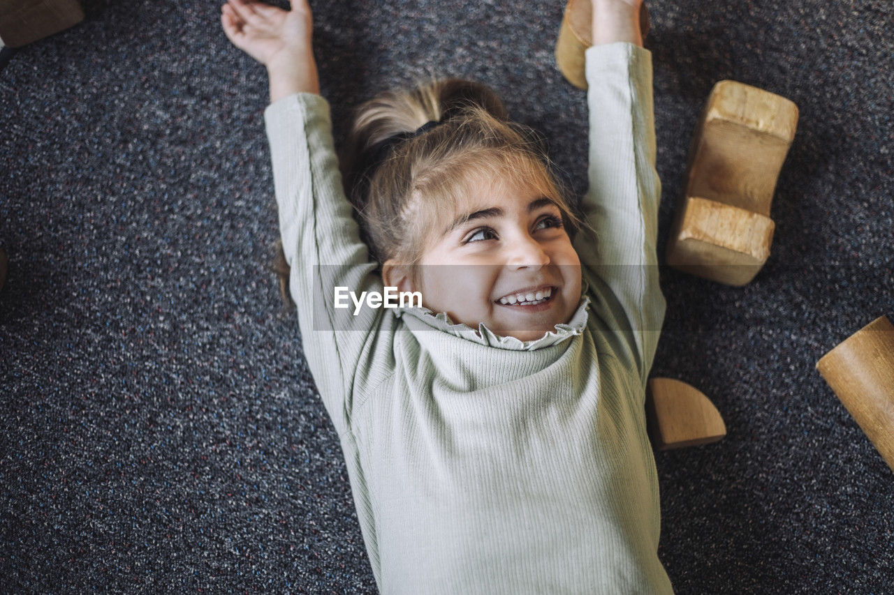 Directly above view of happy girl lying down with arms raised in classroom