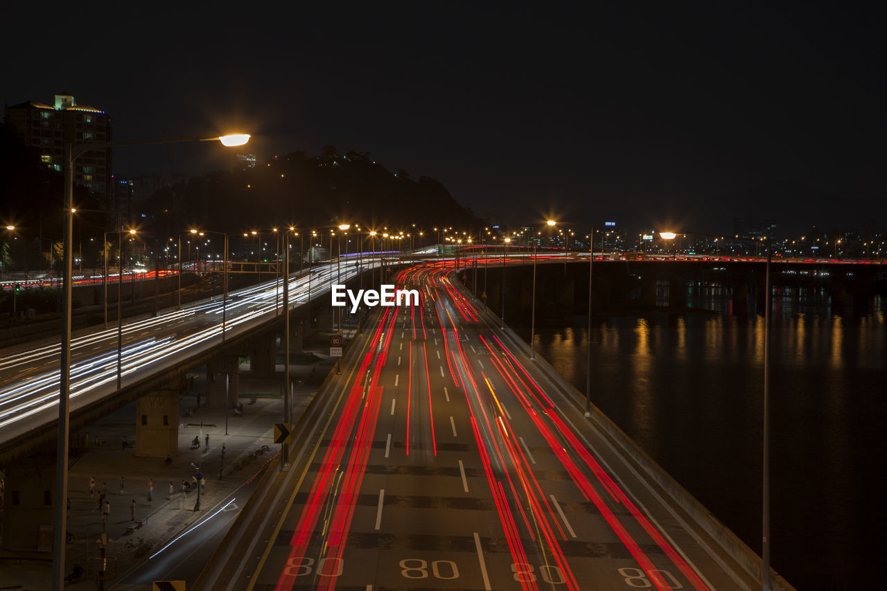 High angle view of light trails on road by river in city at night