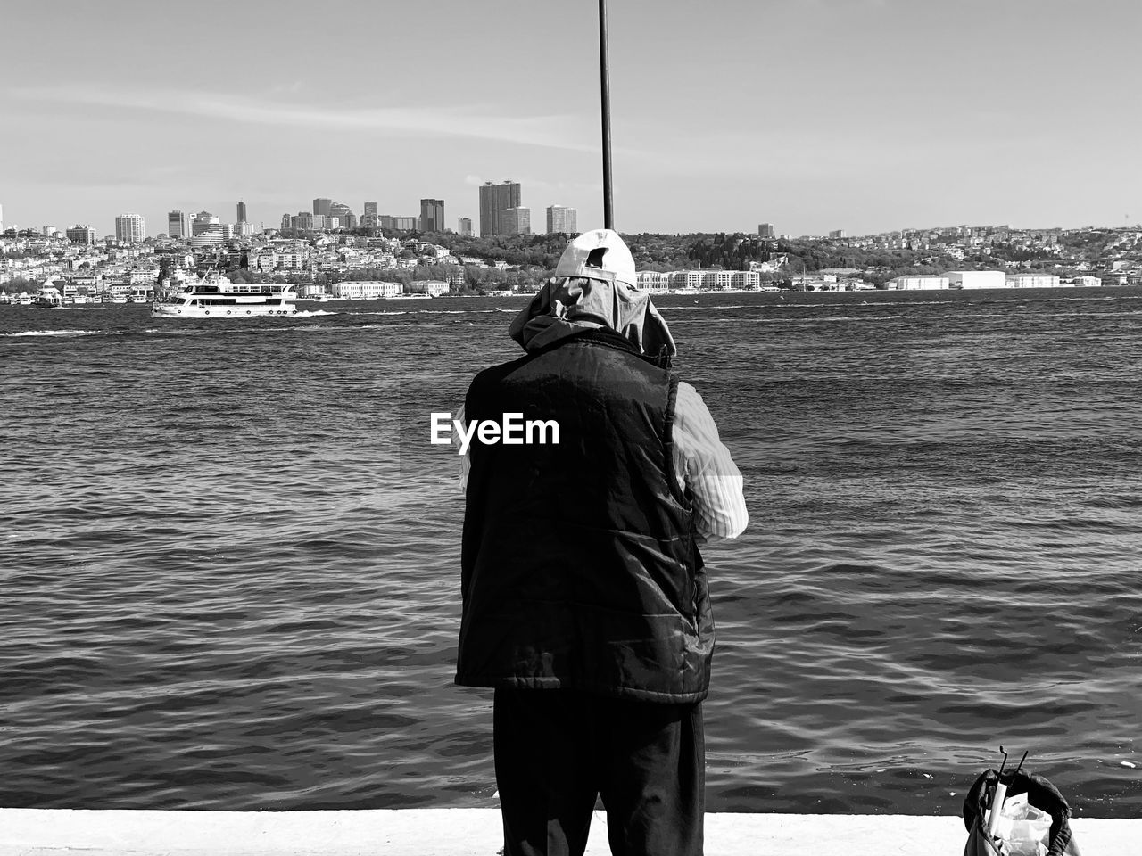 REAR VIEW OF MAN LOOKING AT SEA AGAINST CITY