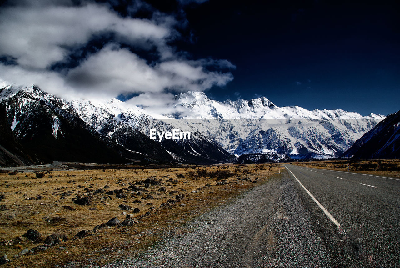 Road leading towards snowcapped mountains against sky