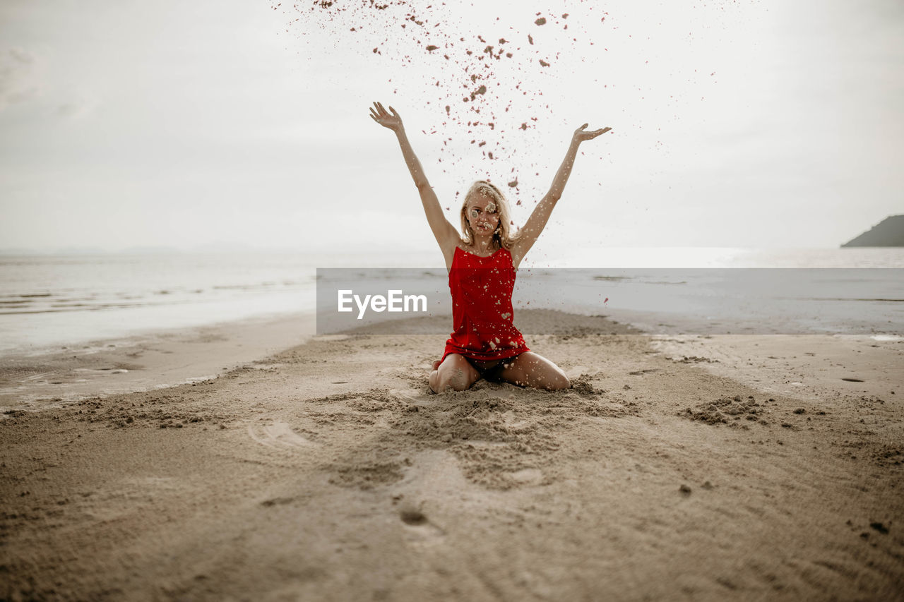 land, beach, one person, sea, water, sand, sky, nature, arm, holiday, limb, arms raised, happiness, red, women, adult, trip, vacation, motion, human limb, full length, morning, child, emotion, carefree, leisure activity, childhood, clothing, enjoyment, fun, horizon over water, smiling, vitality, female, white, cheerful, person, environment, outdoors, relaxation, horizon, young adult, lifestyles, joy, day, beauty in nature, wave, tranquility, sunlight, summer, positive emotion, arms outstretched, portrait, front view, barefoot