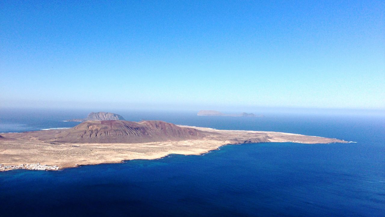 Aerial view of island and sea against blue sky