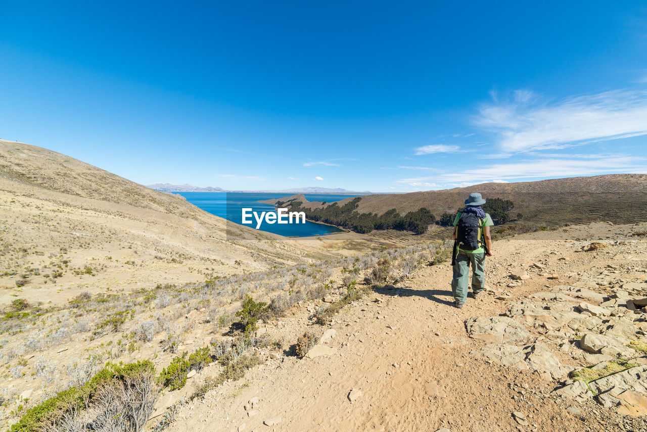 Rear view of man walking on landscape against sky