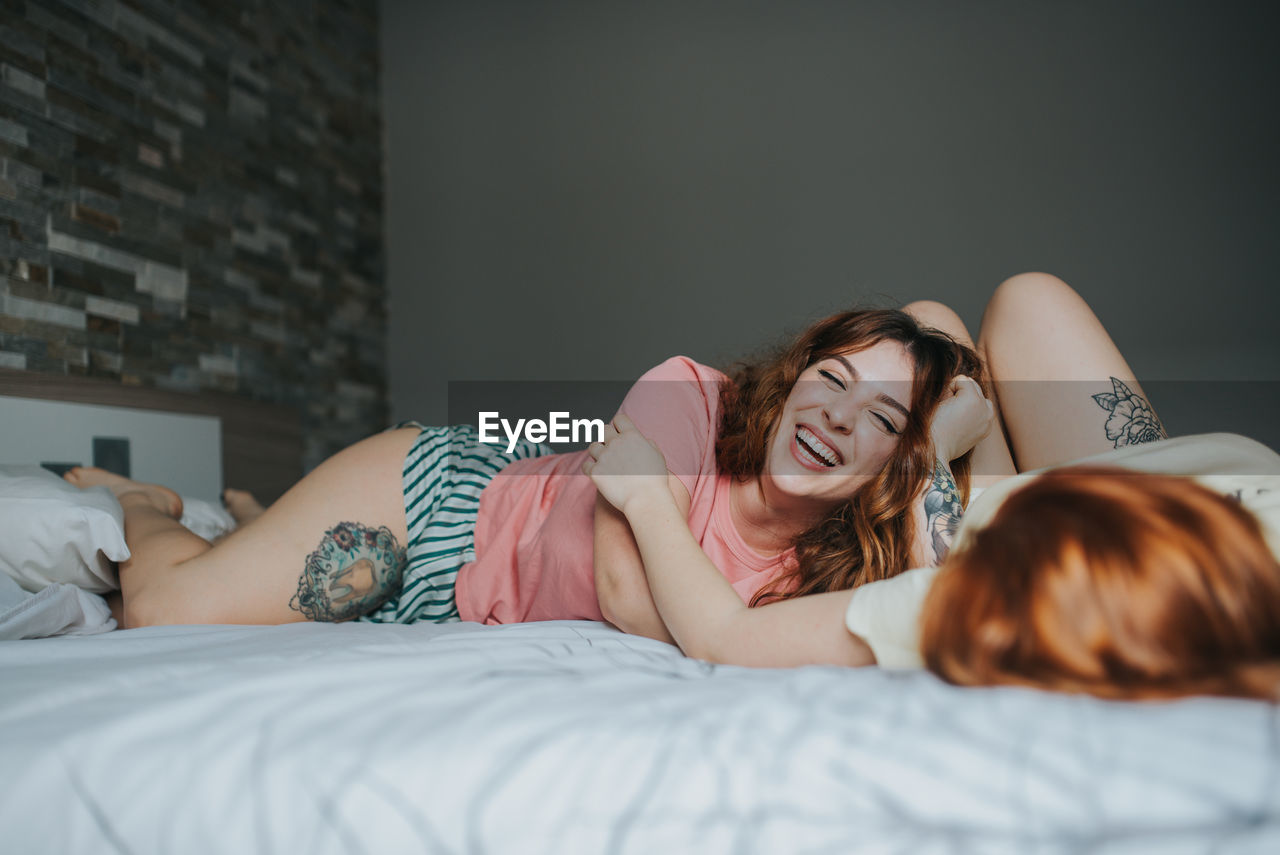 Crop young female girlfriends in pajamas relaxing on bed in bedroom