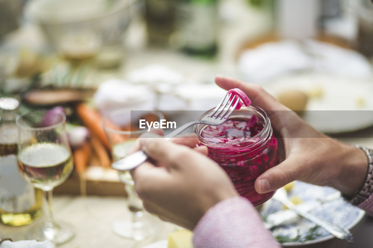 Cropped image of man removing pickle from jar at table during dinner party