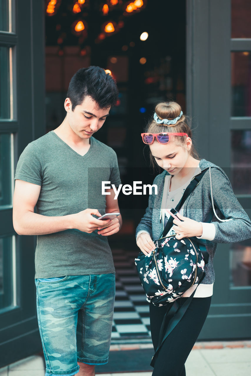 Smiling teenage friends using mobile phone in city