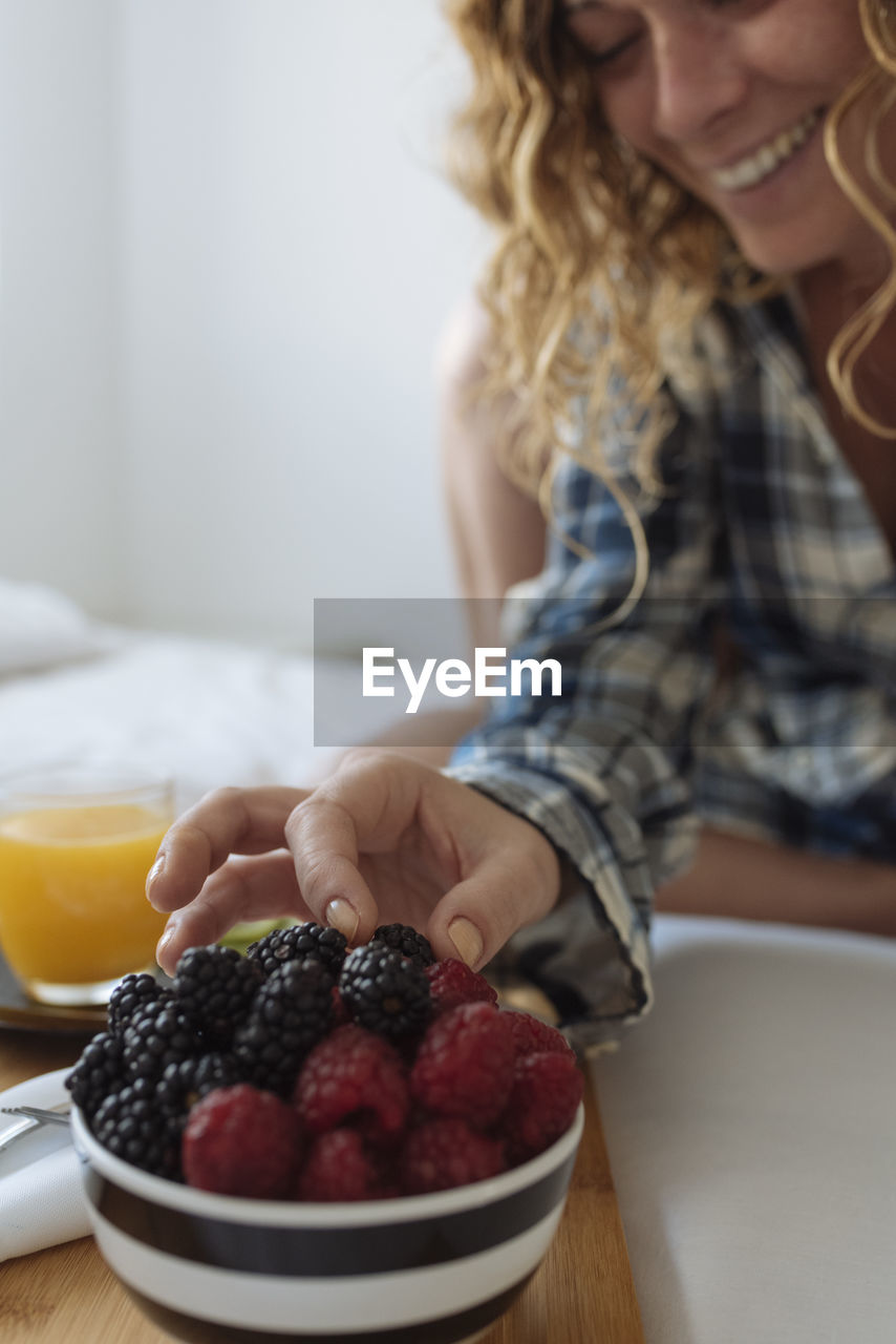 Close up of woman's hand taking a berry of a breakfast tray on the bed