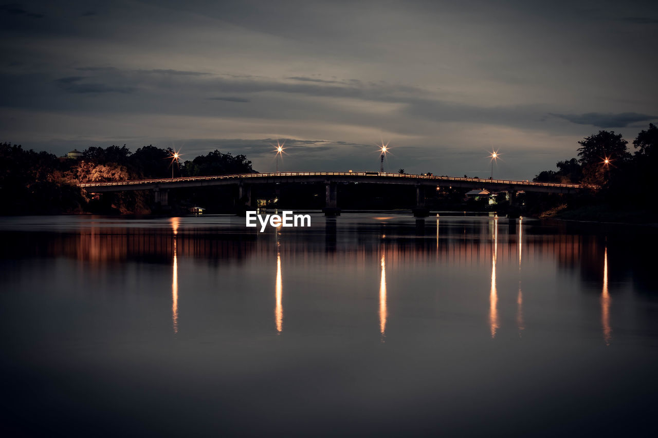 Old railway bridge over river at night with reflection in ratchaburi thailand