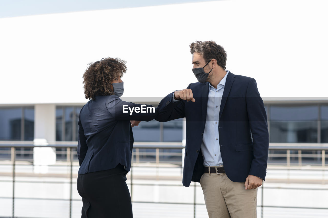 Colleagues giving elbow bump while greeting at office building terrace