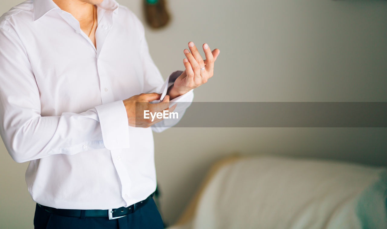 Midsection of woman holding mobile phone while standing on bed