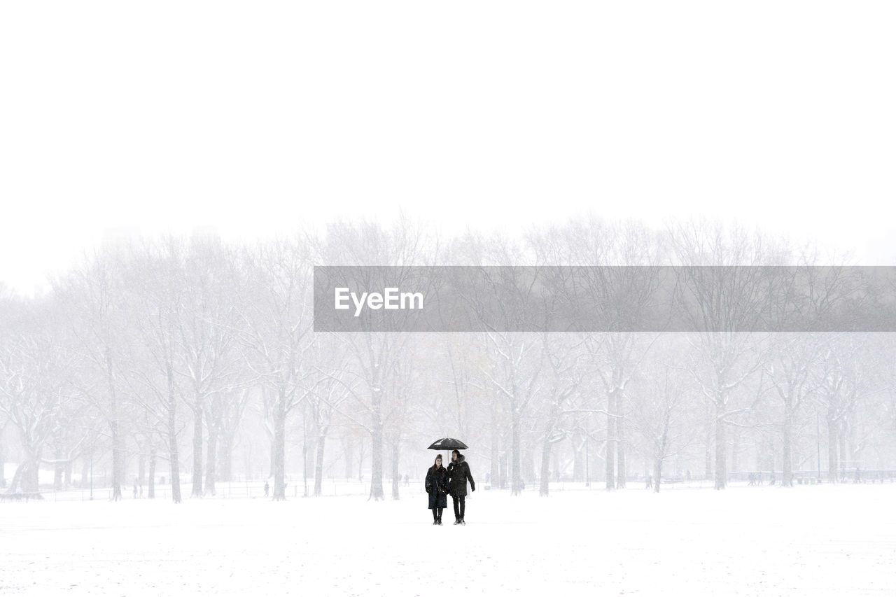 REAR VIEW OF MAN ON SNOW COVERED FIELD