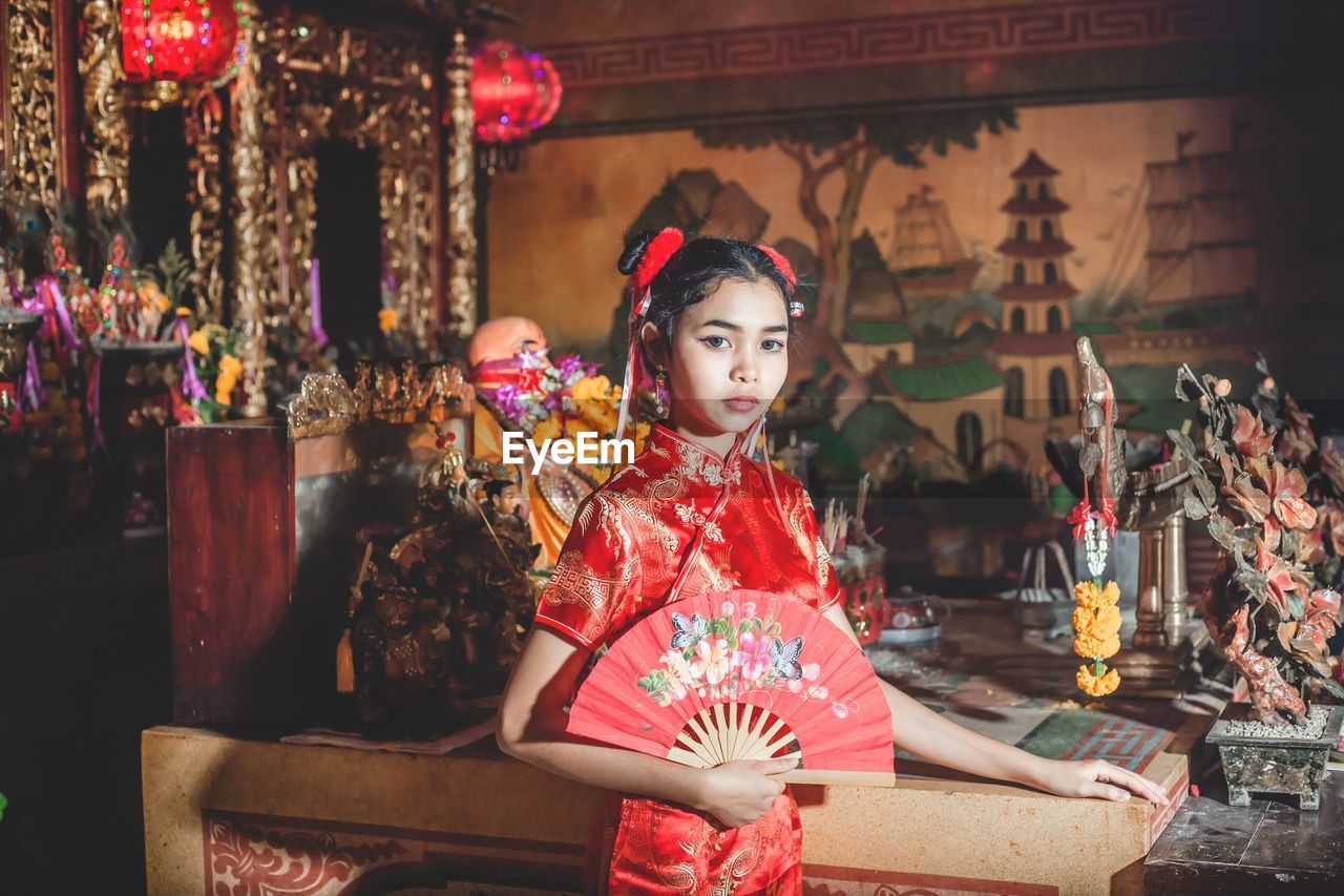 Portrait of girl standing with hand fan in traditional clothing