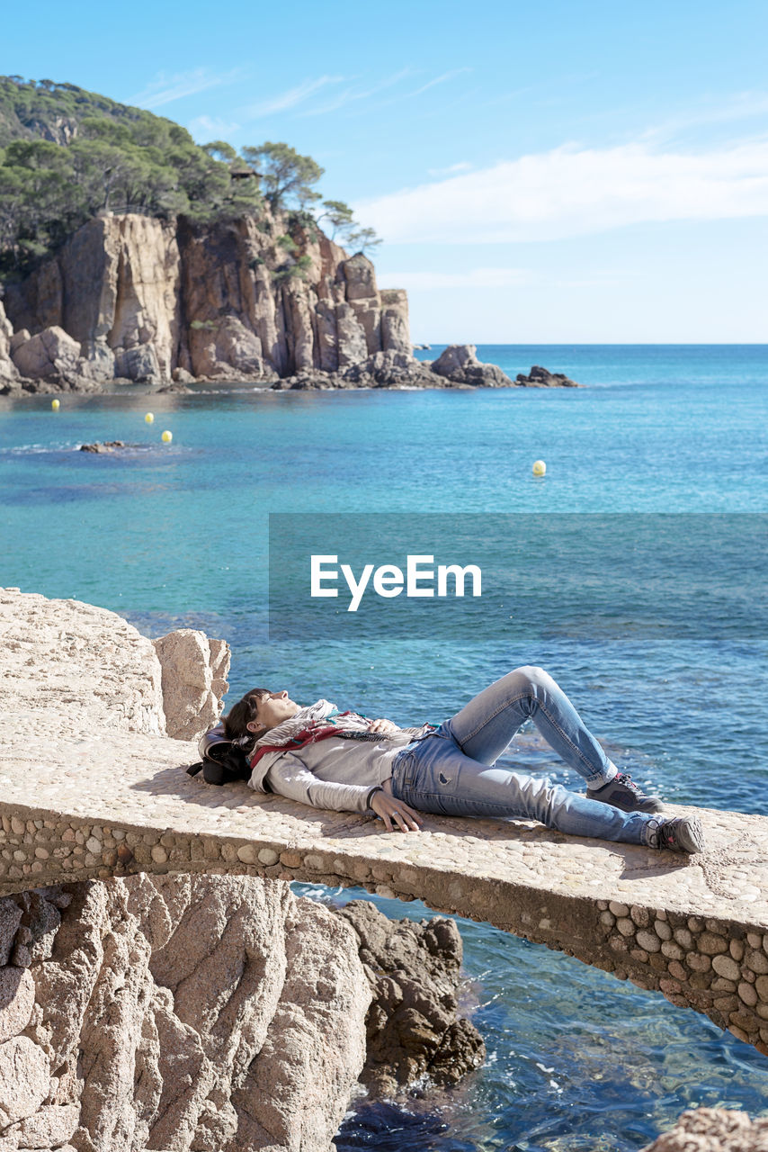 Rear view of a woman relaxing in front of blue sea, lying on bridge