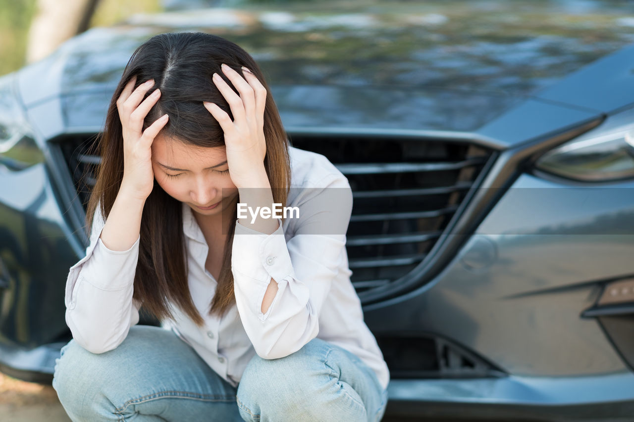 Tensed woman with head in hands crouching against car