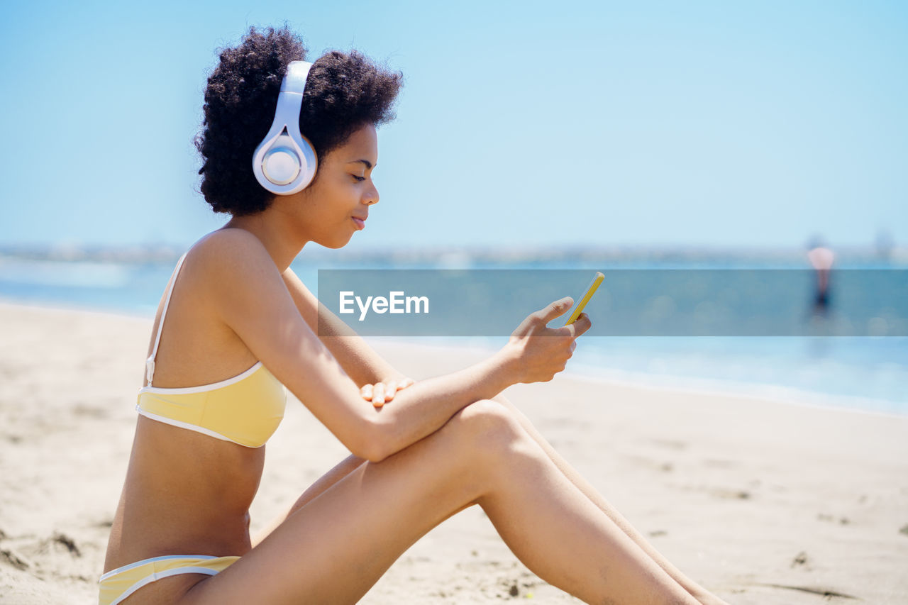 rear view of woman sitting at beach against sky