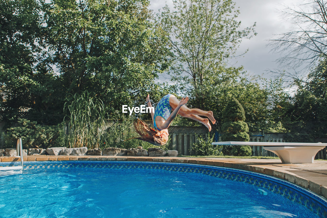 Girl jumping in swimming pool against trees