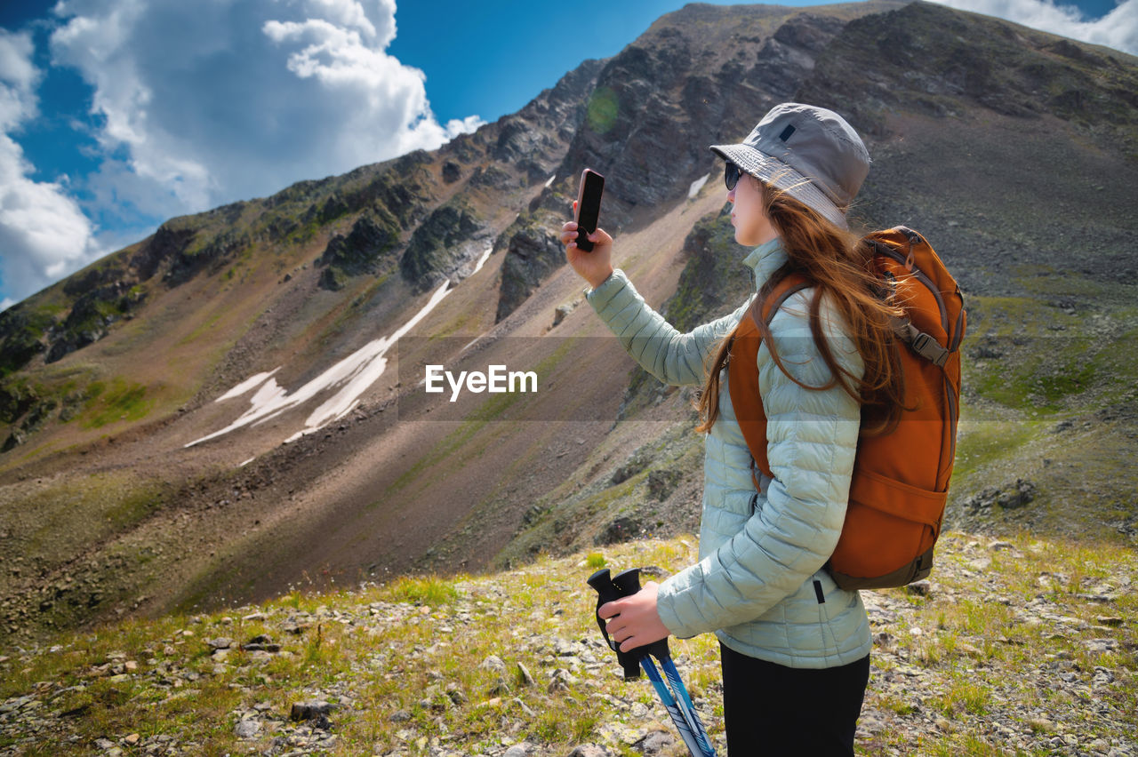 Side view of female blogger taking selfie on smartphone while hiking, discovering wild lands on