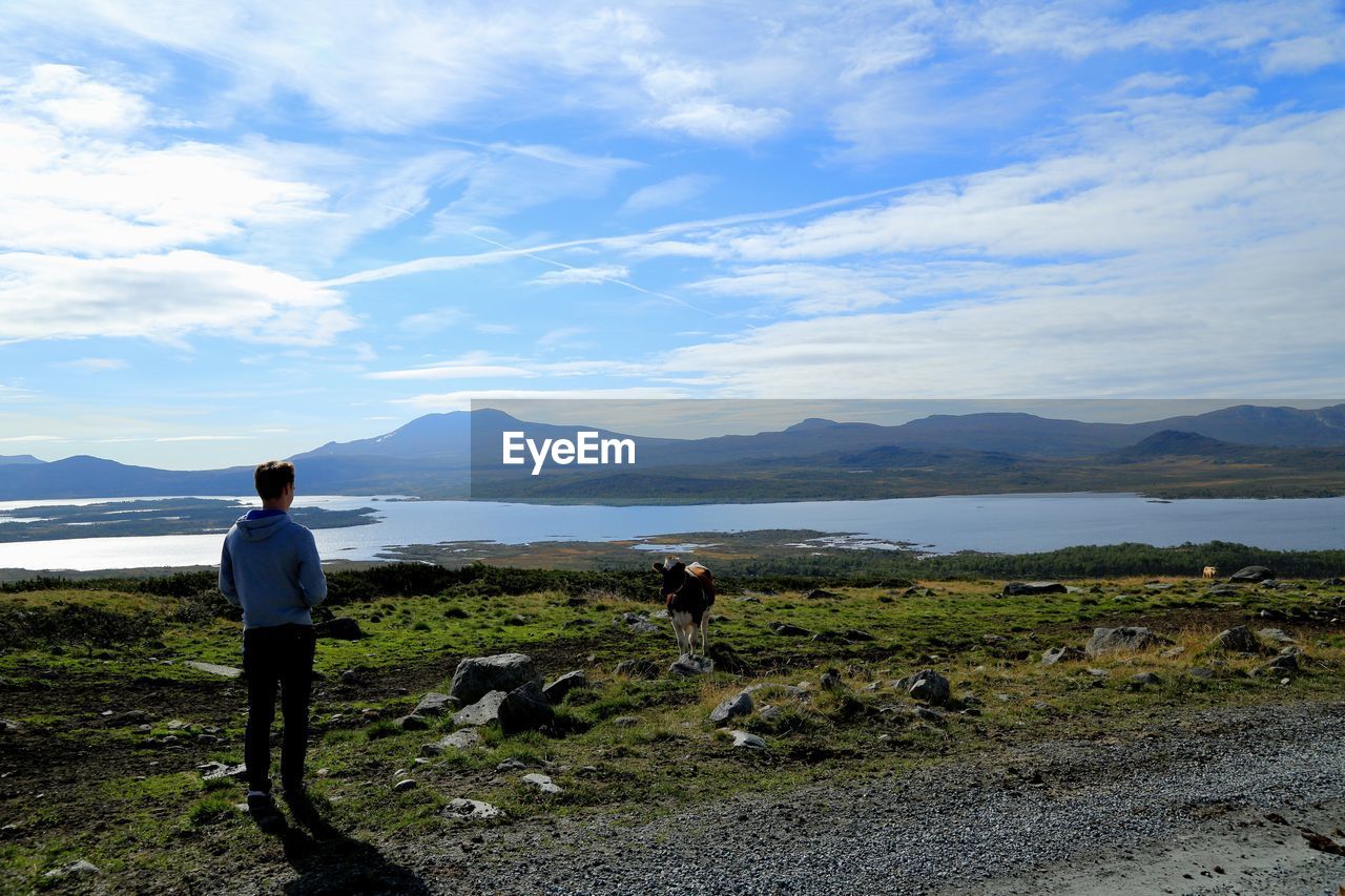 Rear view of teenage boy looking at lake and mountains against sky