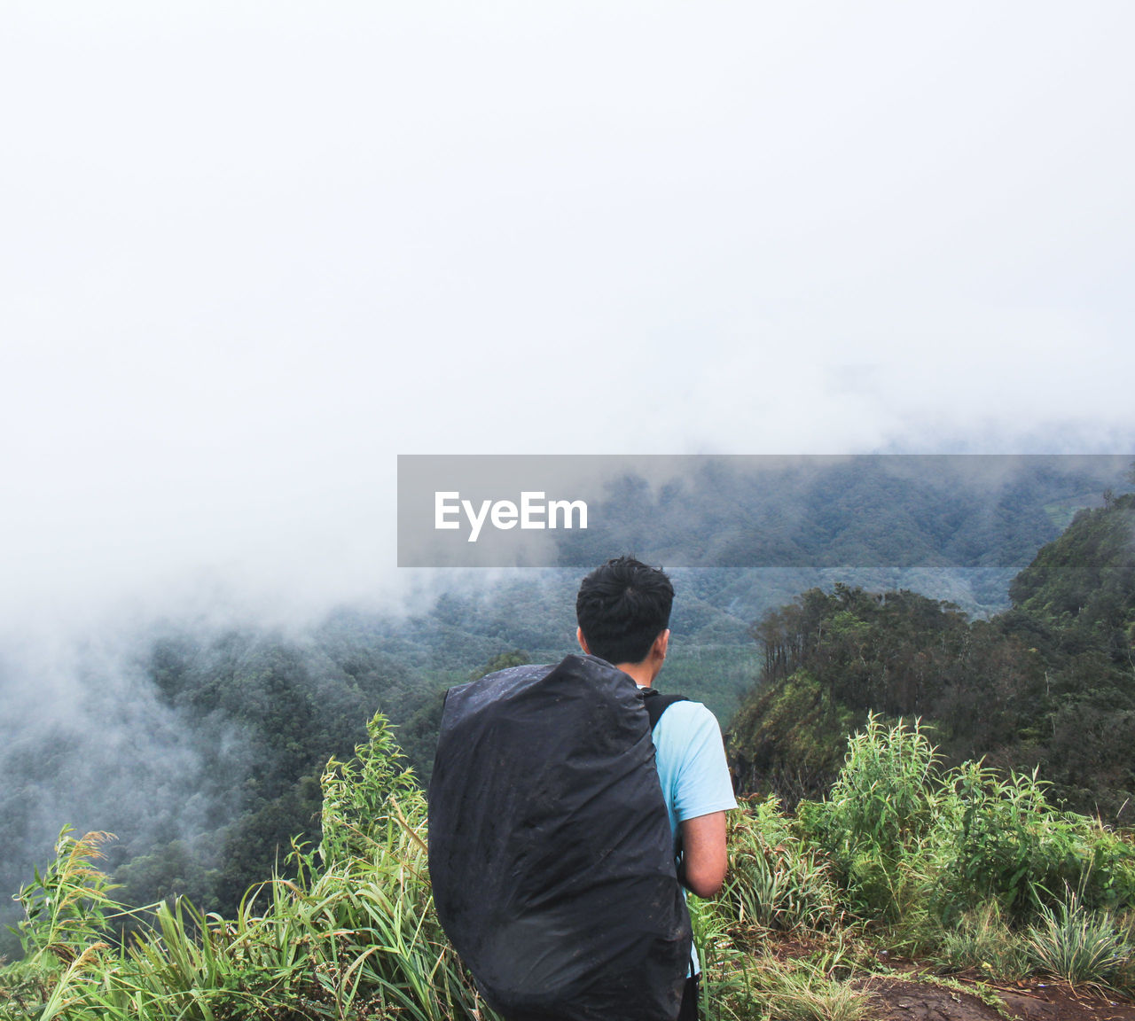 Rear view of backpack man hiking on mountain during foggy weather