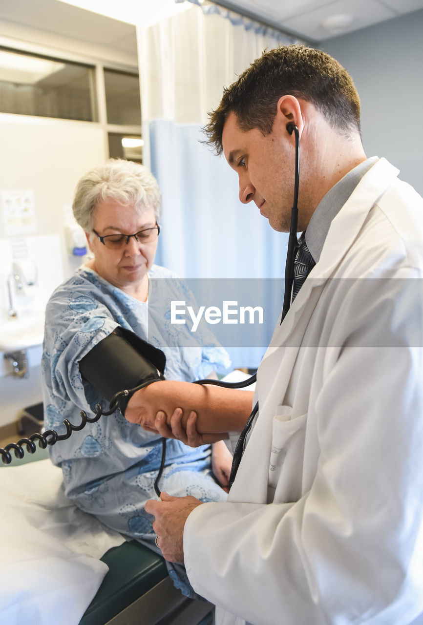 Doctor taking blood pressure of an older patient in clinical setting.