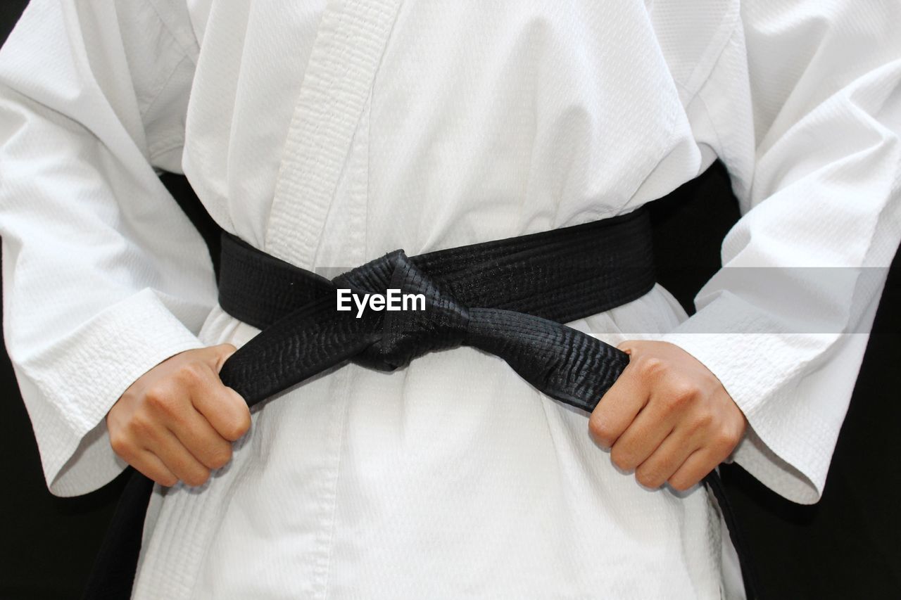 Midsection of athlete wearing black belt against black background