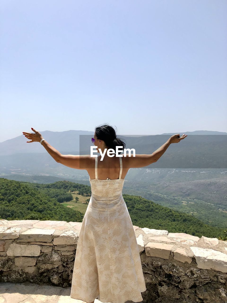 Rear view of woman with arms outstretched standing on mountain against sky
