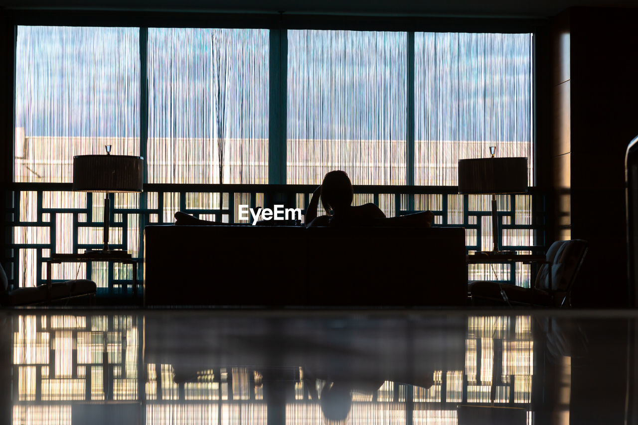 Rearview of silhouette woman sitting at the window in the lobby