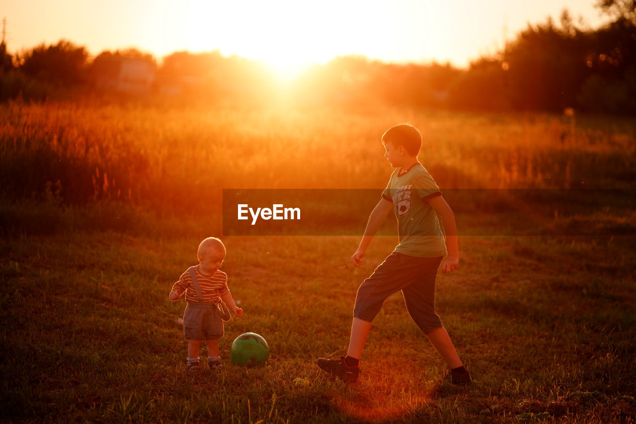 Boy plays ball with his younger brother at sunset