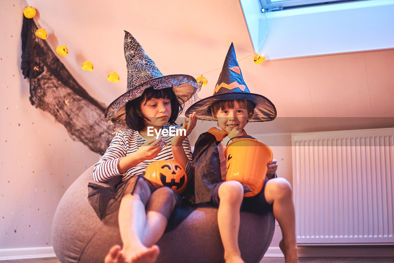 Cheerful boys and a girl in suits eat sweets from pumpkin buckets