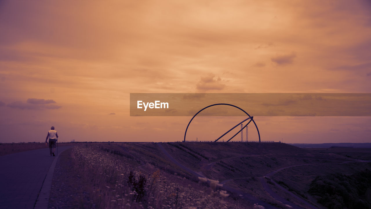 MAN CYCLING ON ROAD AGAINST SKY DURING SUNSET