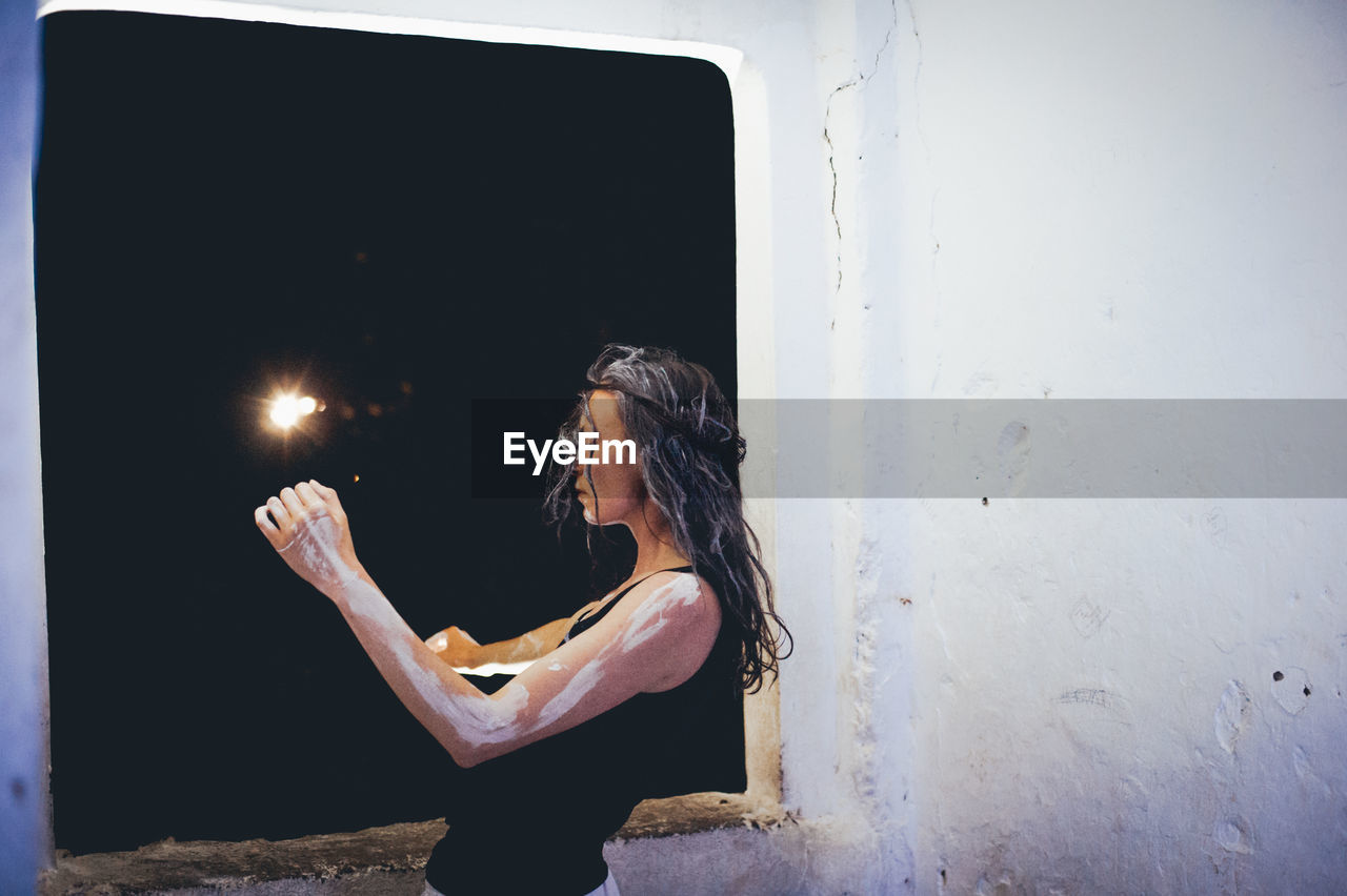 Woman covered in paint while standing against window at night
