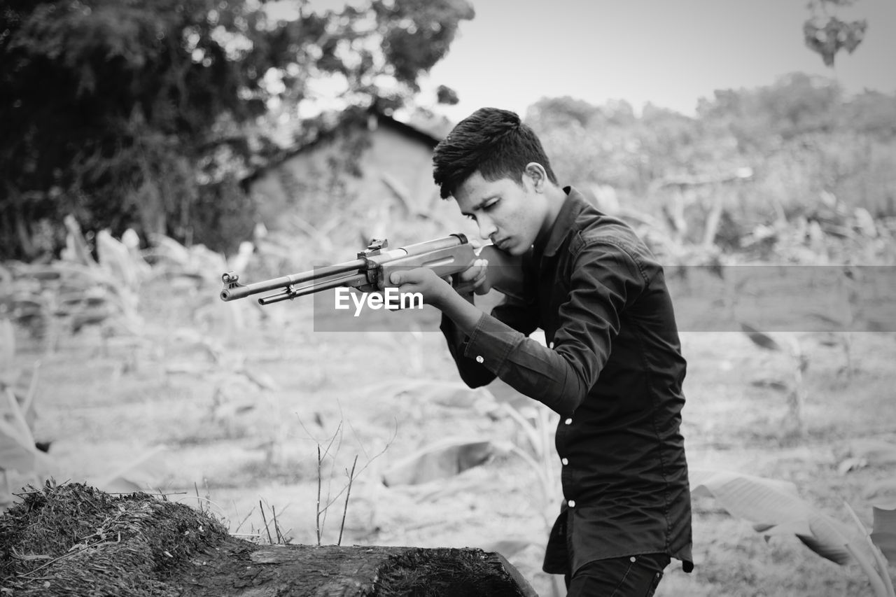 Young man aiming with rifle while standing at farm