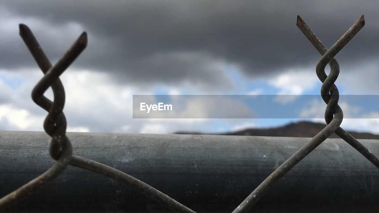 Close-up of barbed wire against cloudy sky