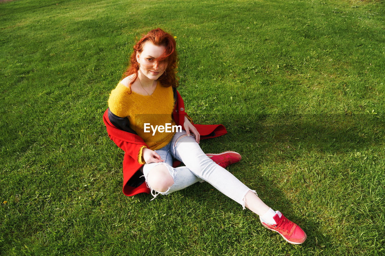 Young woman sits on green grass in spring park