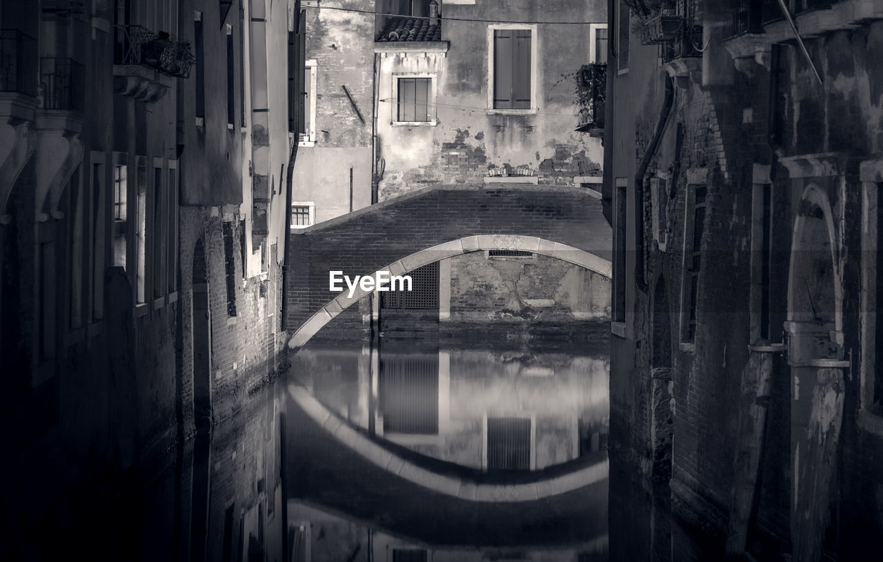 BRIDGE OVER CANAL AMIDST BUILDINGS IN CITY