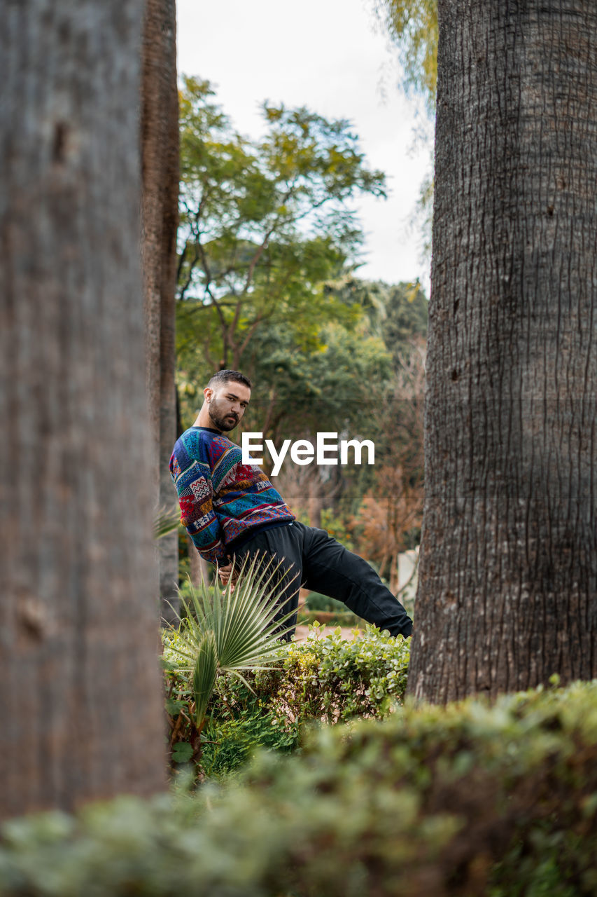 Caucasian model standing in between palm trees in a public park