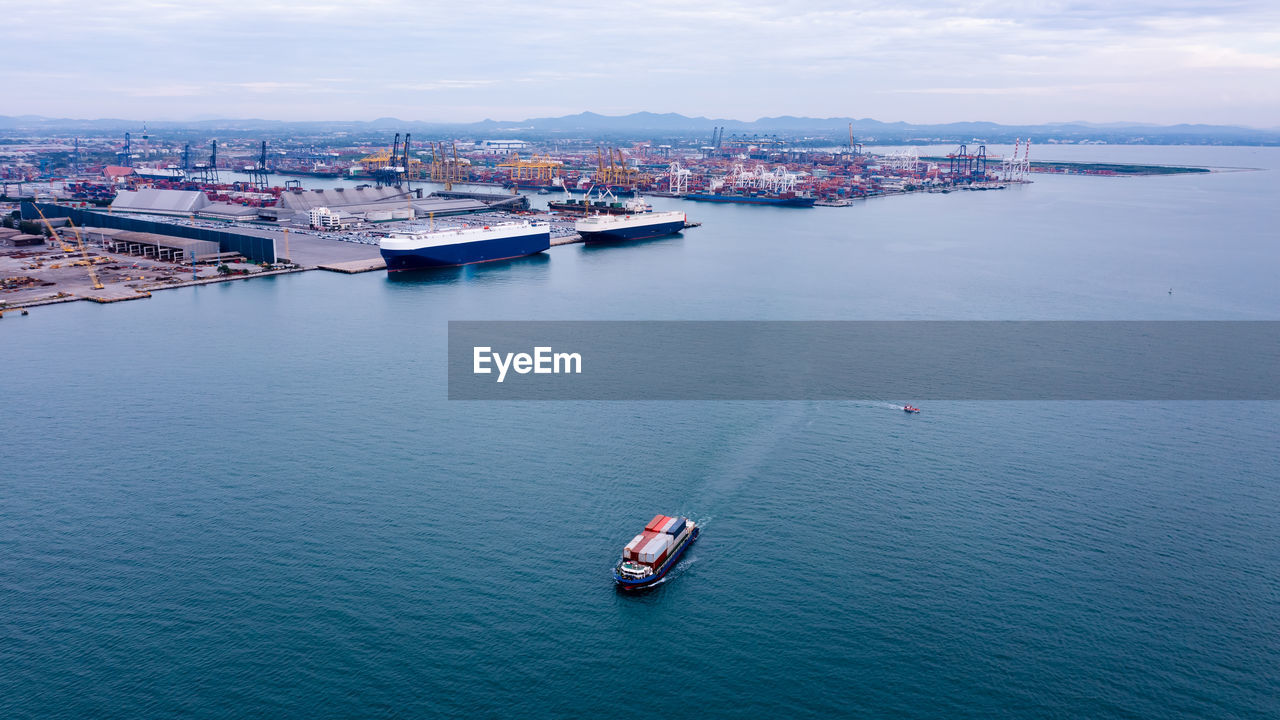Small container ship sailing in sea and shipping port background photograph aerial view from drone 