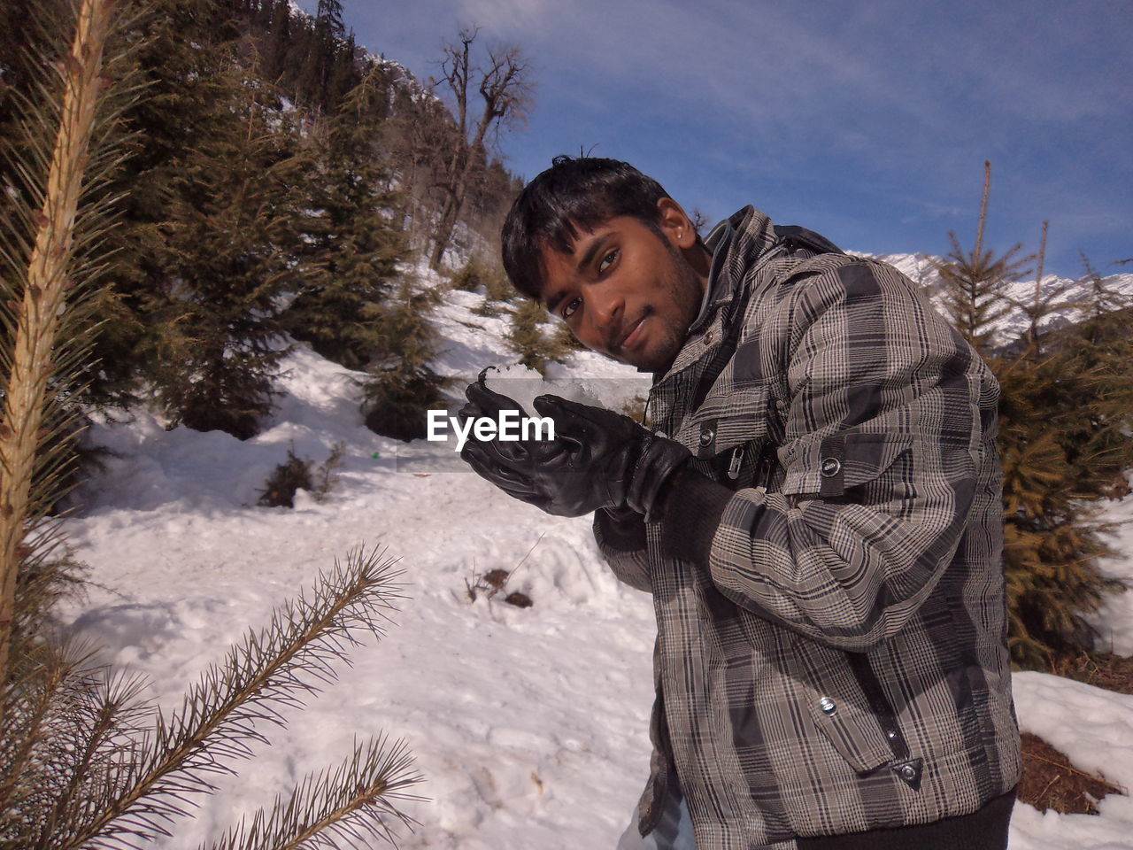 Portrait of young man holding snow on mountain during winter