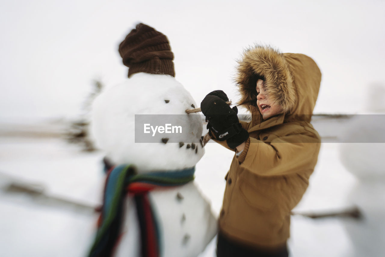 Boy making snowman while standing on field