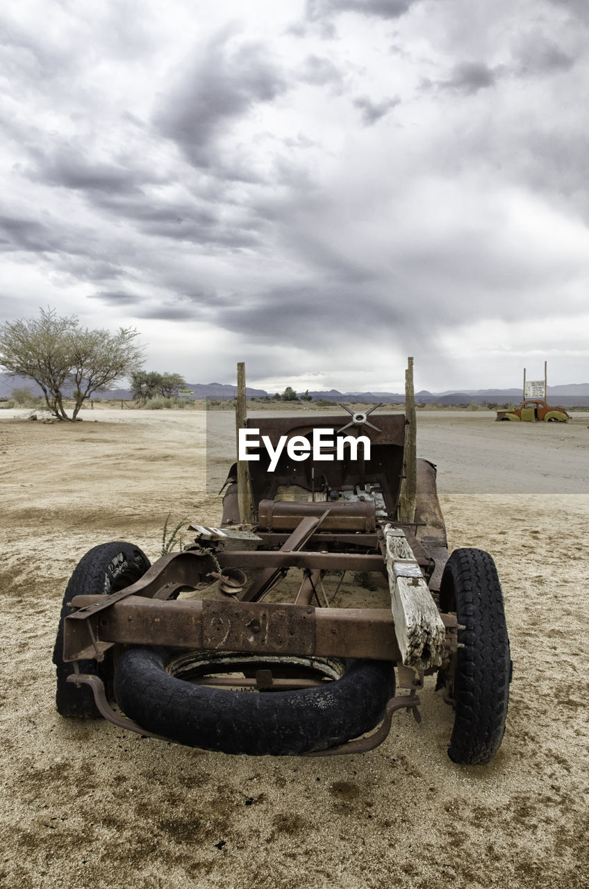 ABANDONED VINTAGE CAR ON FIELD AGAINST SKY