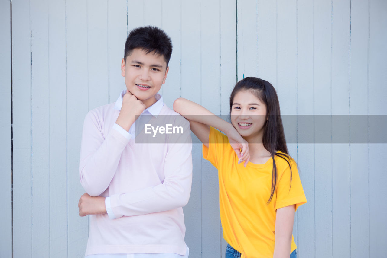 Portrait of smiling boy and girl standing against wall