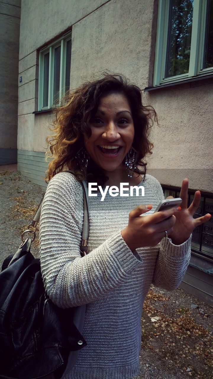 Portrait of happy woman text messaging against building in city