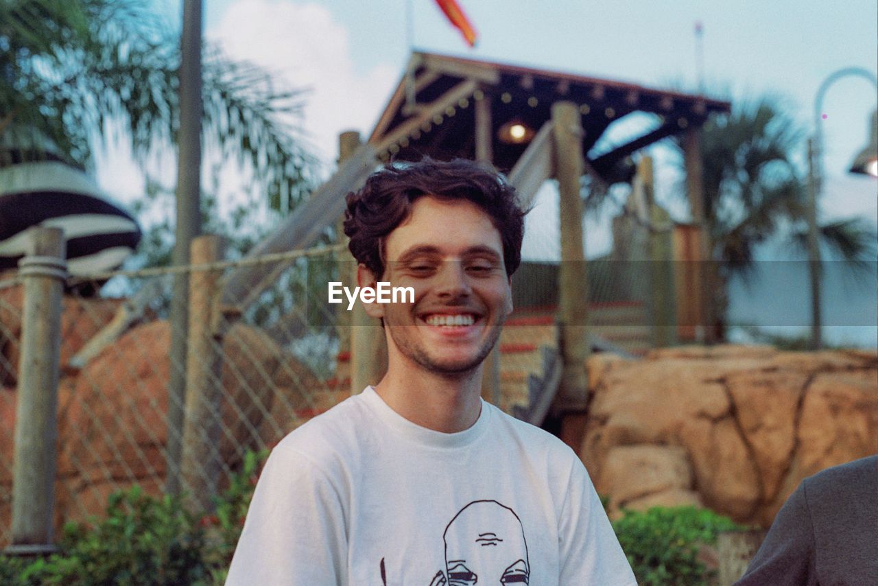 PORTRAIT OF SMILING YOUNG MAN AGAINST BUILDING