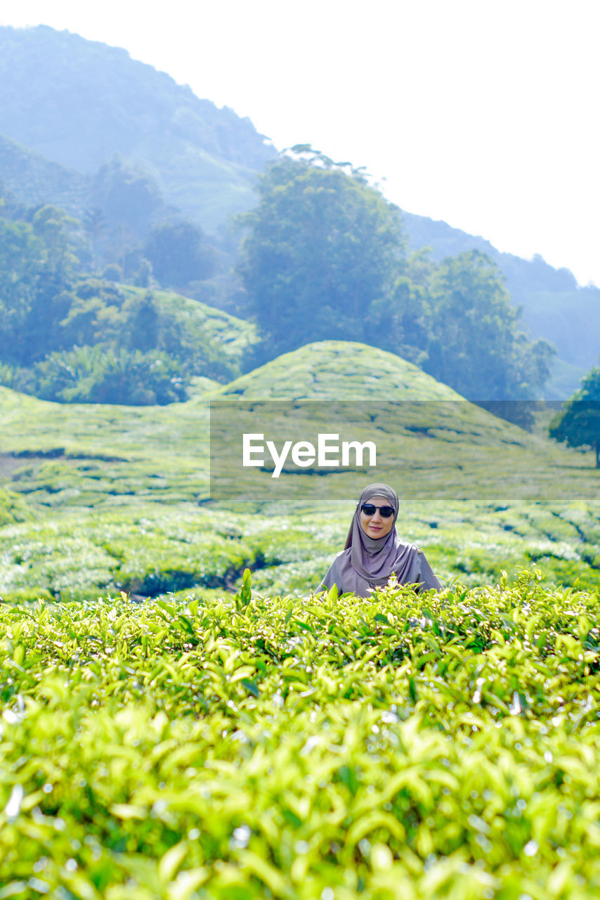Portrait of woman standing amidst tea plantation against mountain