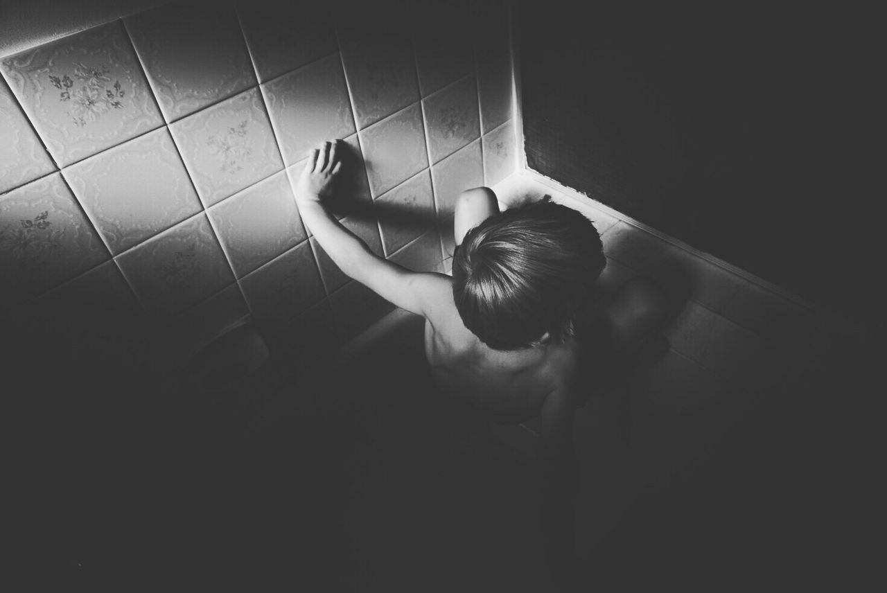 High angle view of naked boy crouching in bathroom