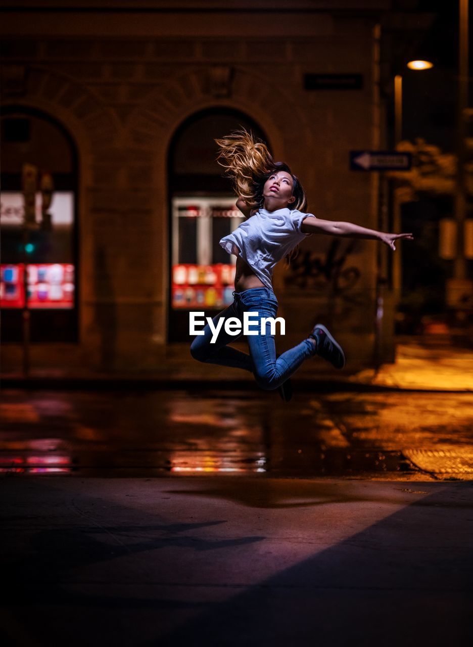 SIDE VIEW OF MAN JUMPING AGAINST ILLUMINATED CITY