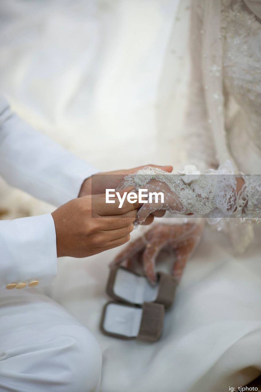 Midsection of groom putting ring in bride finger