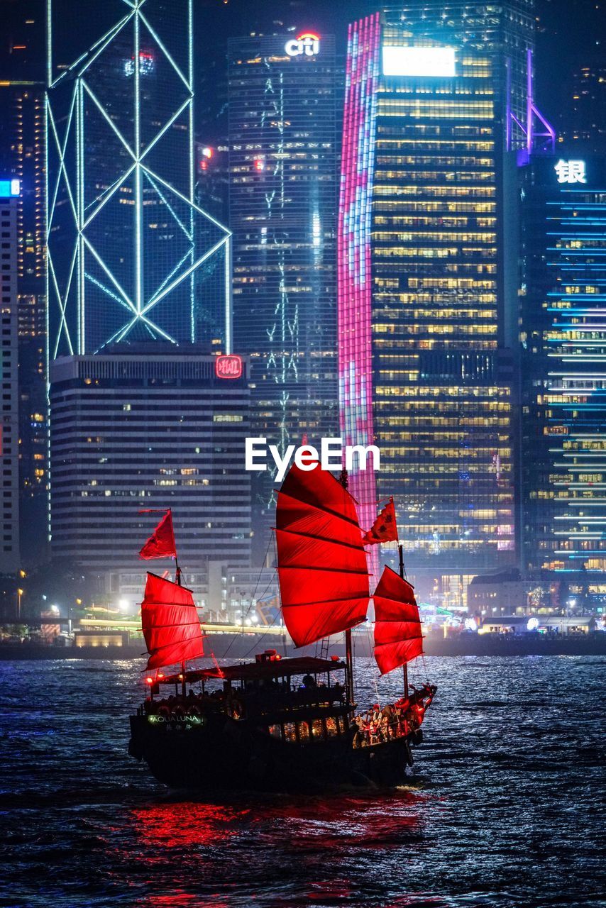 Red boat in river against illuminated buildings at night