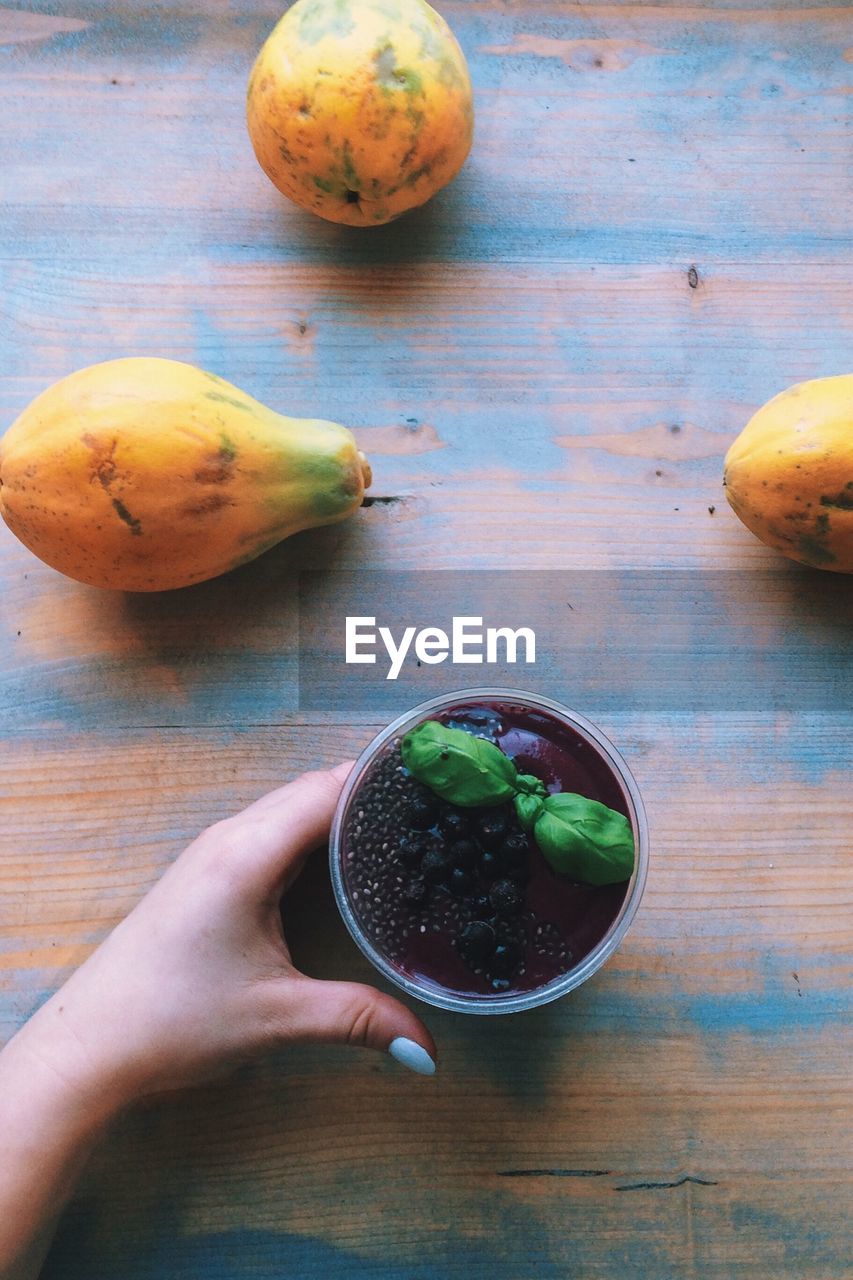 Cropped image of hand holding flower pot on table with papayas